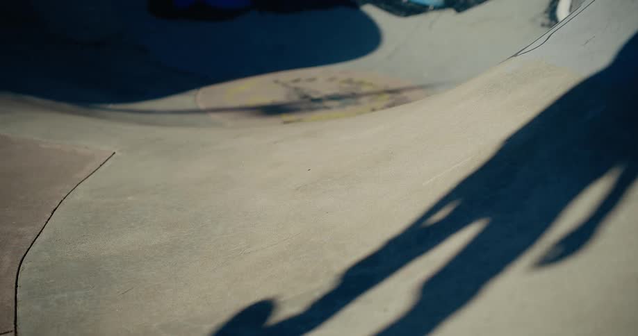 Shadow of person with skateboard casts over curved concrete surface in late afternoon