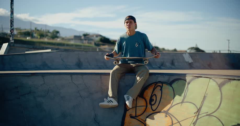 Person sits on bowl edge holding colorful skateboard