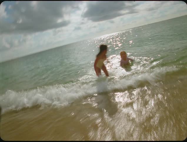 Children playing in shallow water with gentle waves under a partly cloudy sky