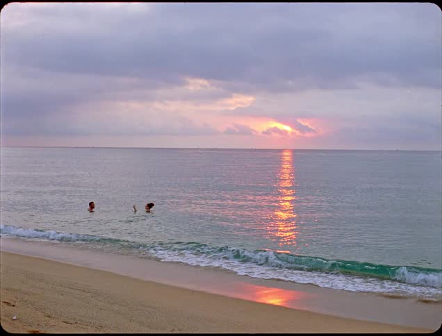 Two adults a man and a woman swim together in the ocean near the beach at sunset enjoying their time in the water