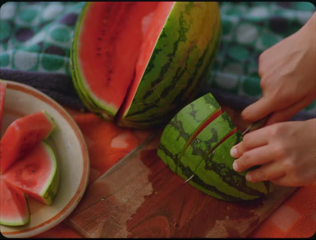 A person cuts fresh watermelon into slices on a wooden board