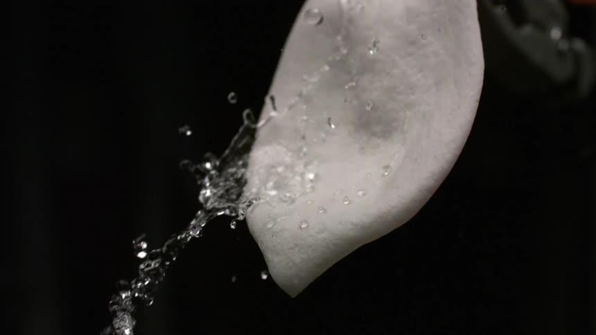 A close view of a stream of water splashing onto a smooth gray object and quickly running off its surface against a black backdrop
