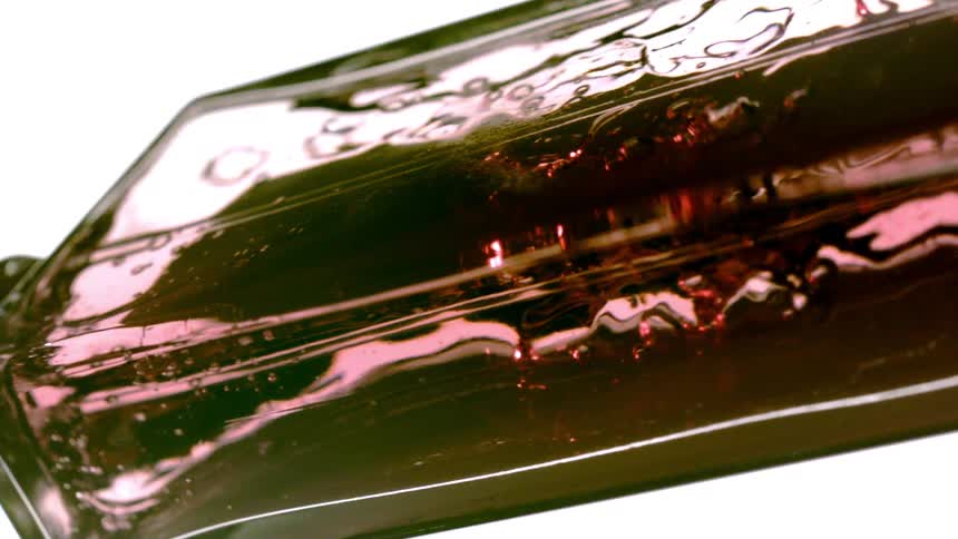 Reddish liquid with suspended bubbles swirls inside transparent container under intense light
