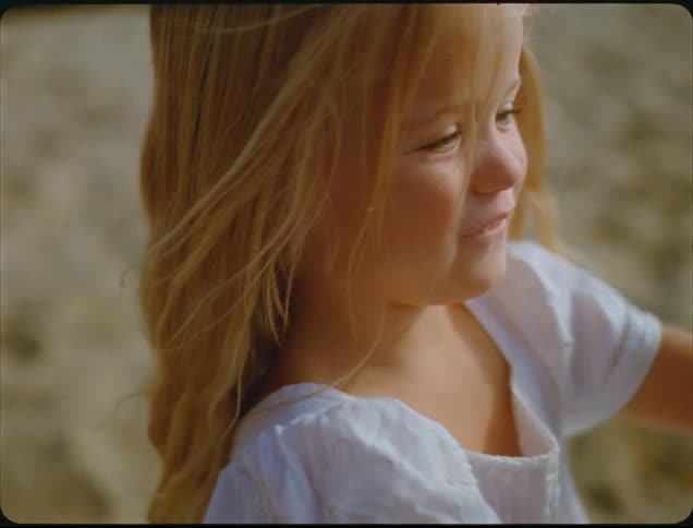 Child in white dress smiles and plays with hands against softly blurred lighttoned background