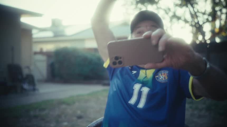 The man wearing a sports jersey cheers at his phone in the yard