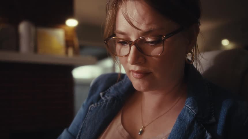 The video begins with a closeup of a womans hands pressing buttons on a calculator surrounded by papers and a keyboard suggesting she is working on finances the camera then tracks up to reveal the woman wearing glasses and a denim jacket looking do