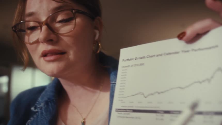 A woman is talking as she gives a presentation in an office pointing at a graph on a sheet of paper