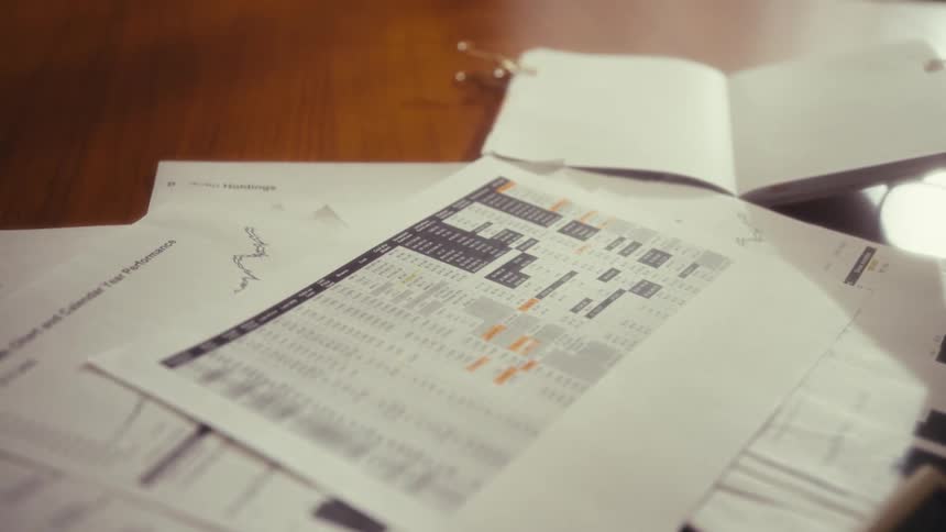 A woman is in an office at a desk using a calculate as she looks at graphs on papers