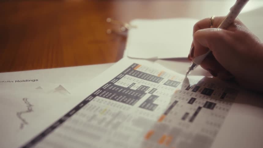 A person reviews and marks financial documents on a desk