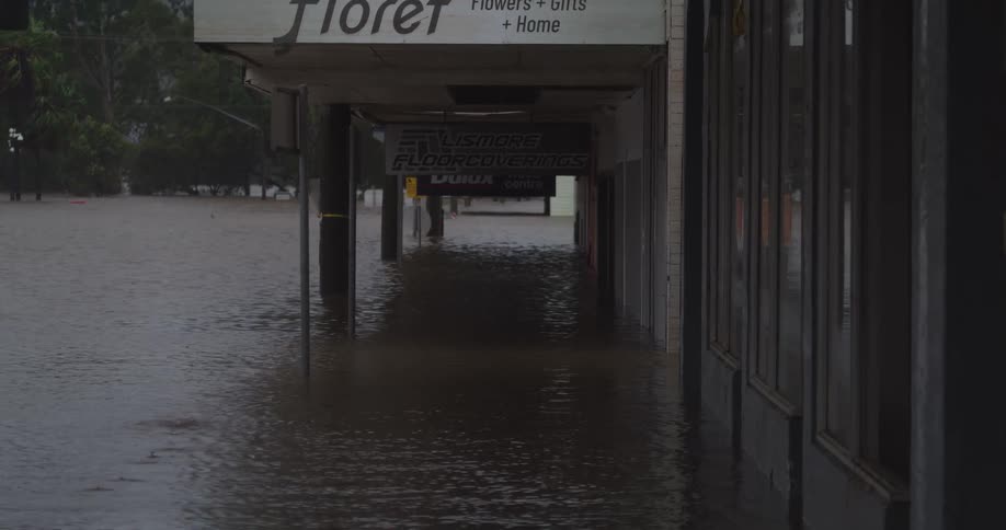 Flooded commercial street reflects storefronts and signs in urban flood scene