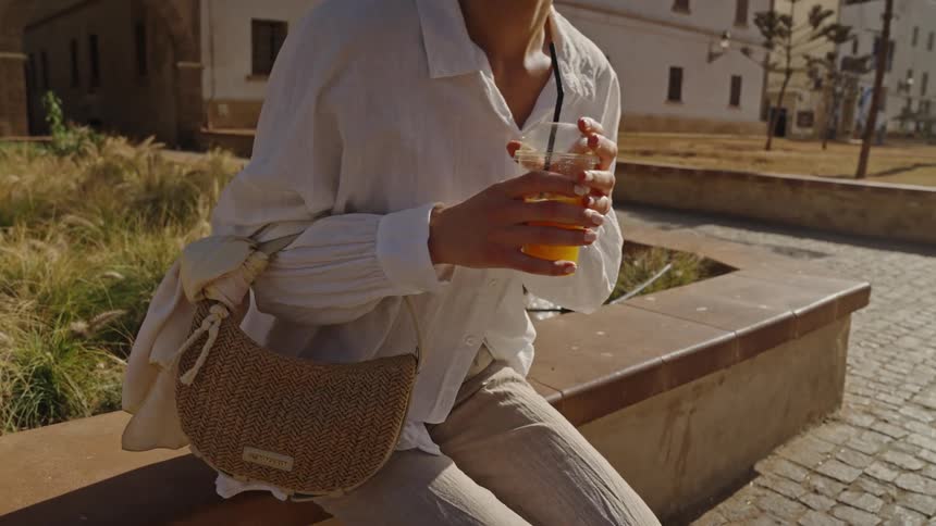 A woman stands up with her drink in front of a building
