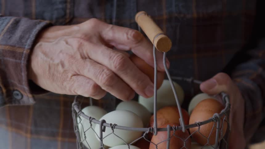 The man lifts an egg from the basket
