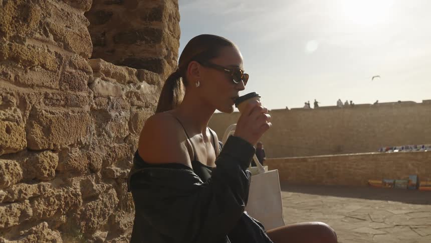 A woman sits outside drinking her coffee as two men walk by