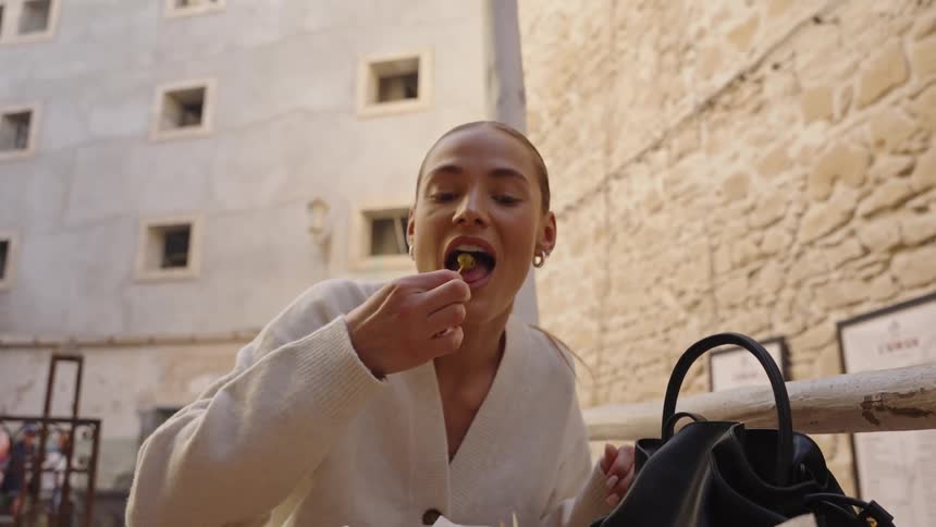 The woman eats an olive at the outdoor eating area