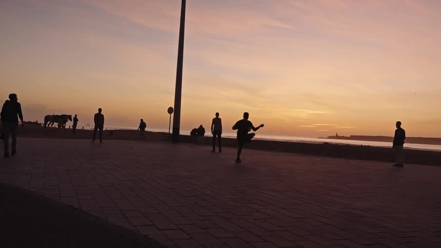 People play ball on waterfront promenade beneath orange sunset sky