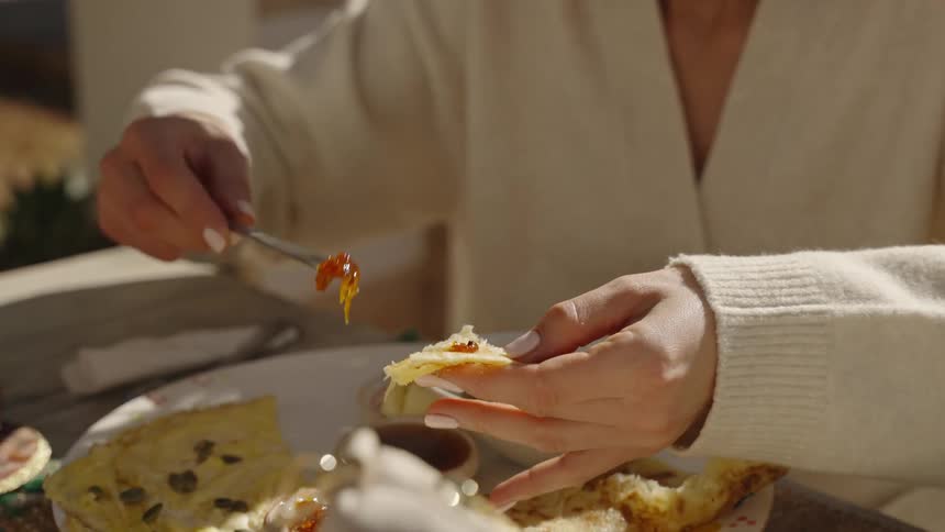 Hands spread jam on bread during an outdoor breakfast