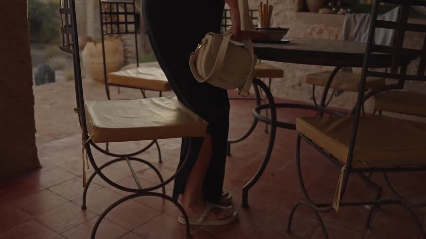 A woman holding a white purse is sitting in a chair that is around a wooden table
