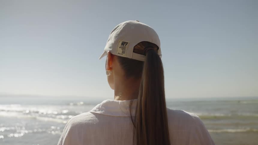 A woman in regular clothes looks back and forth as she stands on a beach