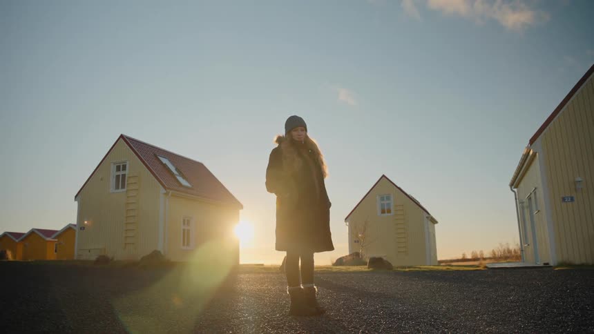 Woman in beanie and dark coat among yellow houses at sunrise or sunset