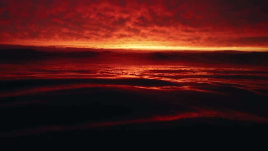 Deep red sunlight reflects on the water as it ripples and waves then goes underwater