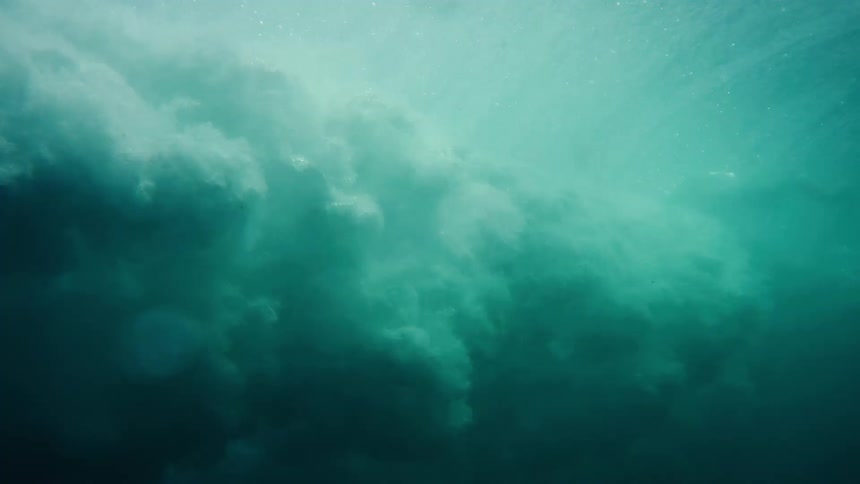 Waves are seen underwater as they roll over and crash