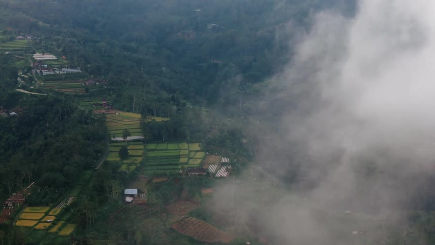 Aerial view of lush green terraced rice fields and village homes on a misty mountainside