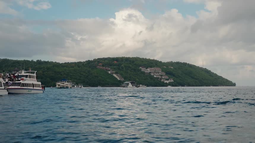 People boarding a white boat next to other boats with a headland on the background during day time