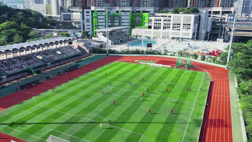 A highangle aerial view tracks slowly to the right over a stadium revealing a soccer match in progress surrounded by a running track and dense city buildings