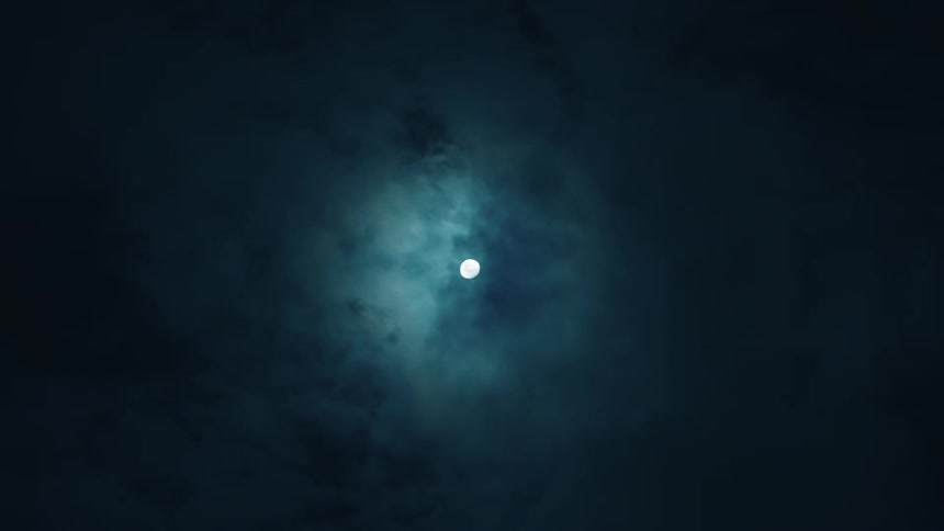 Clouds move across the sky in the moonlight turning them blue