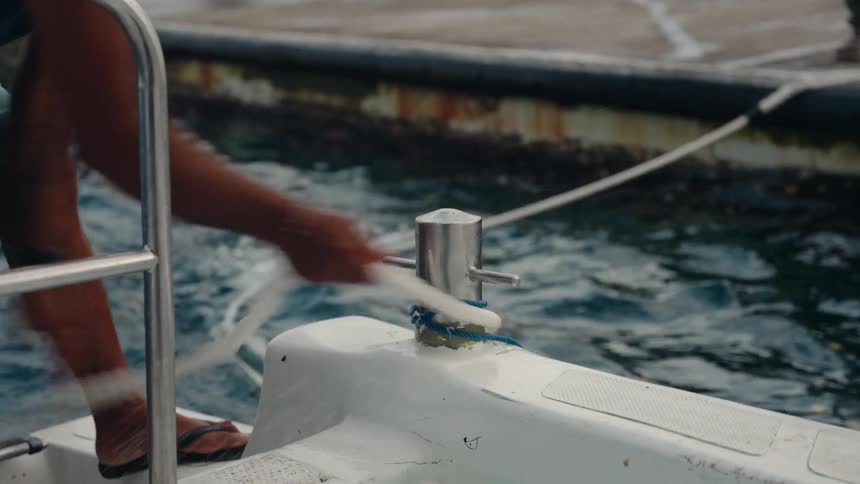 A man rushes to use a rope to dock a boat next to a pier as another person waits