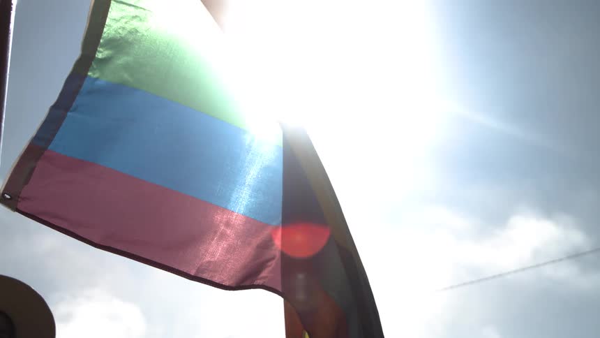 Flag with horizontal colorful stripes waving in the wind with sunlight shining behind