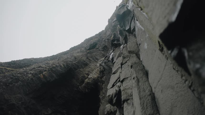 A mountainous rock with jagged rough edges as small rock particles tumble down its surface