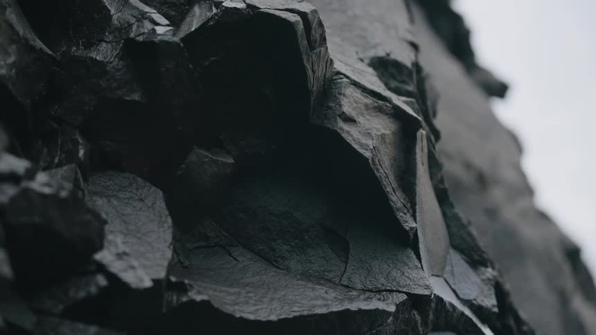 The video presents a closeup static shot of a dark jagged and heavily textured rock or cliff face the material appears wet or naturally dark with clear sharp angles and fissures