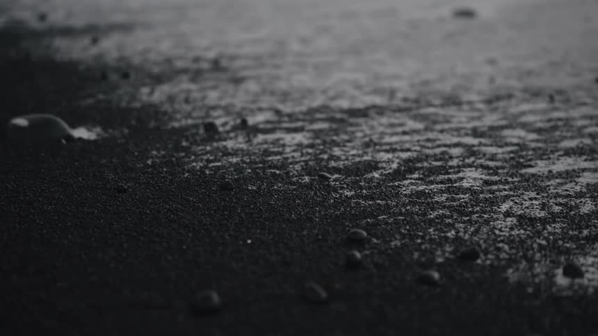 Small water droplets sitting on a textured surface of dark fine gravel as black sand like substance fills in the area