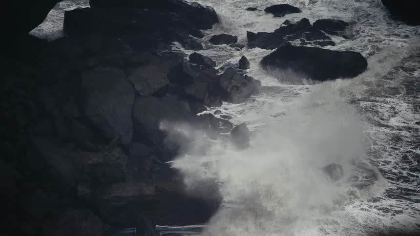 Waves roll in to shore and splash against rocks along the coast