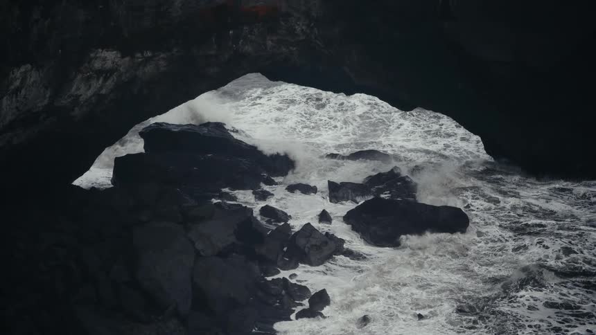 Some waves crashing against rocks on a shore creating white foam on the surface of the water