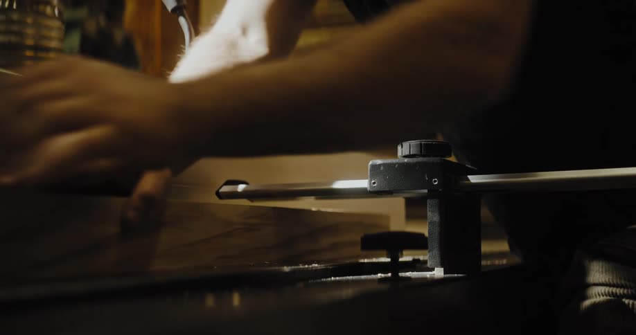 Hands of a male carpenter working a block of wood on a machine indoors during day time