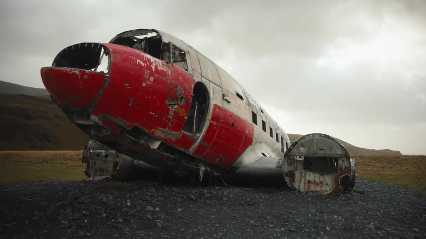 Damaged fuselage of old aircraft on rocky terrain with hills in the background under cloudy sky