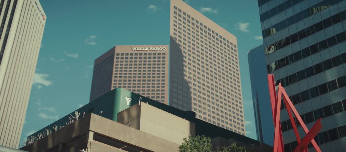 A low angle view of a pedestrian walkway in a downtown area with tall glass and brick corporate skyscrapers visible against a bright blue sky