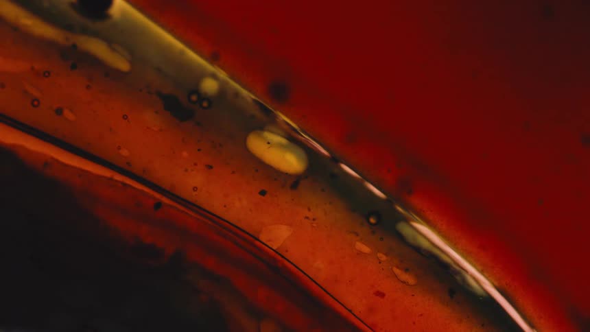 A close abstract view of swirling liquids in red yellow and green creating an oily texture with bubbles and dark lines