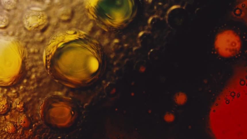This is a macro video showcasing a chaotic mix of oil and liquid creating numerous bubbles and spheres in varying sizes the colors transition from bright yellow and amber on the left to deep reddishbrown and black on the right suggesting a chemical re