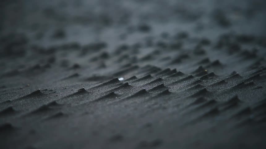 A close view of dark gray volcanic sand featuring small sharp wind blown ridges and peaks across the surface