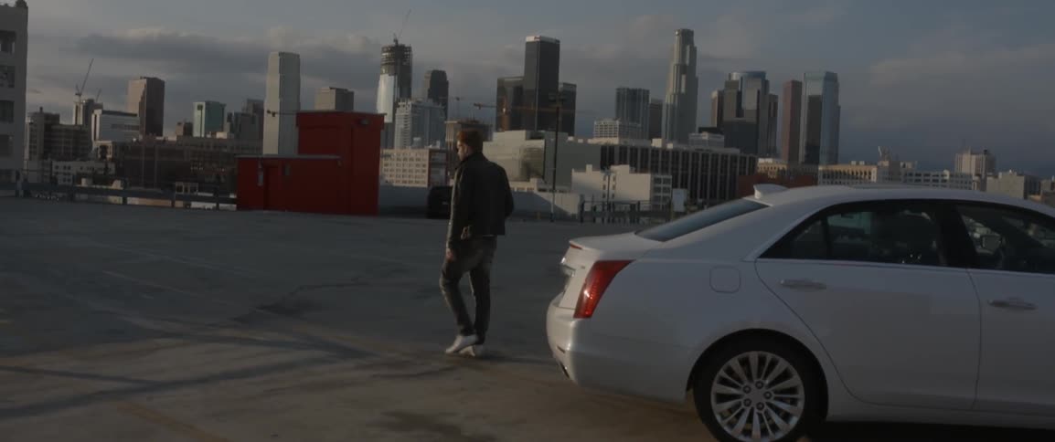 Man gets out of vehicle on the roof of a parking ramp with a city in the background