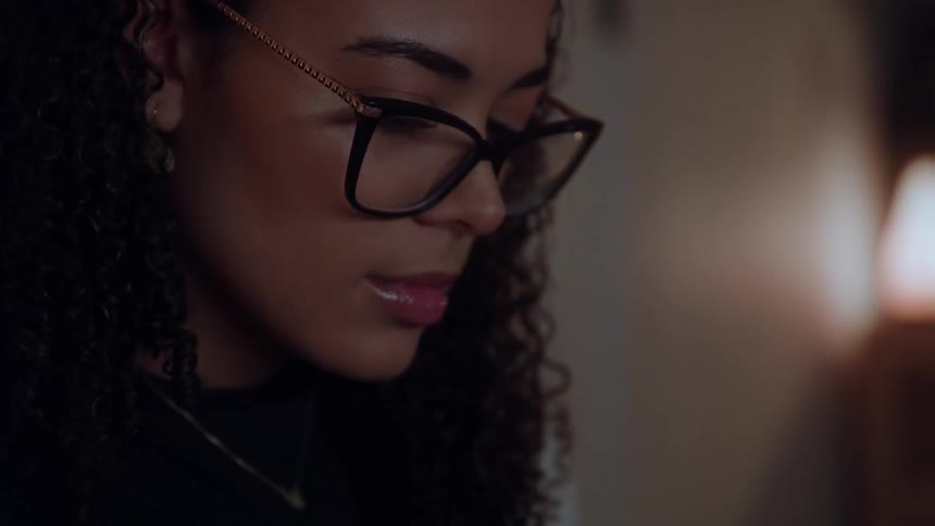 Young woman wearing glasses sitting down indoors and reading