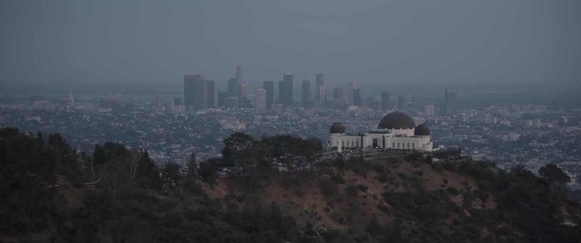 A domed building sits on a hilltop with city skyscrapers in the distance