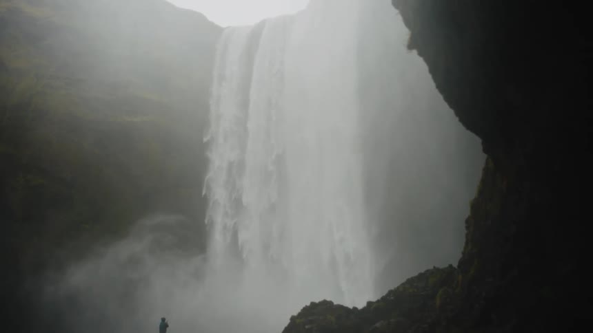 Person standing before large waterfall surrounded by dark rocks and heavy mist