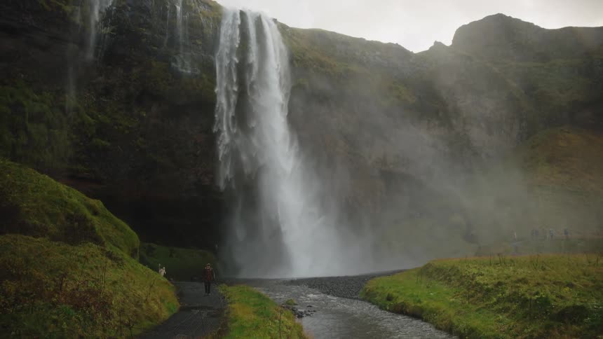Waterfall flows over a mountain cliff as a man walks on the road