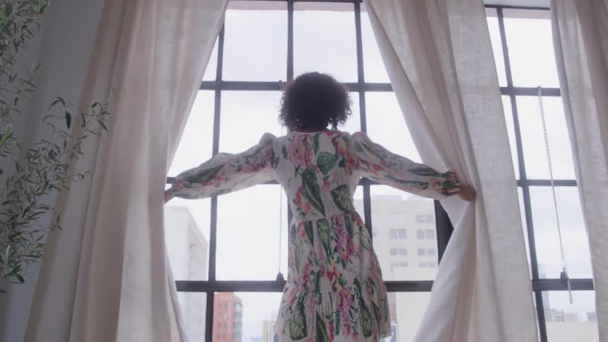 A woman standing before a large window opens the curtains