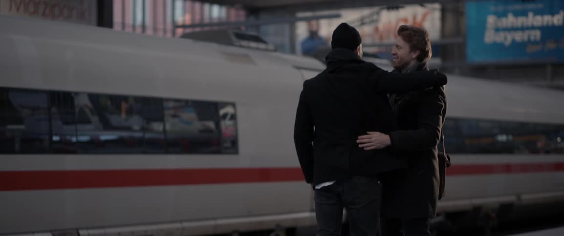 Two men embrace on a train platform
