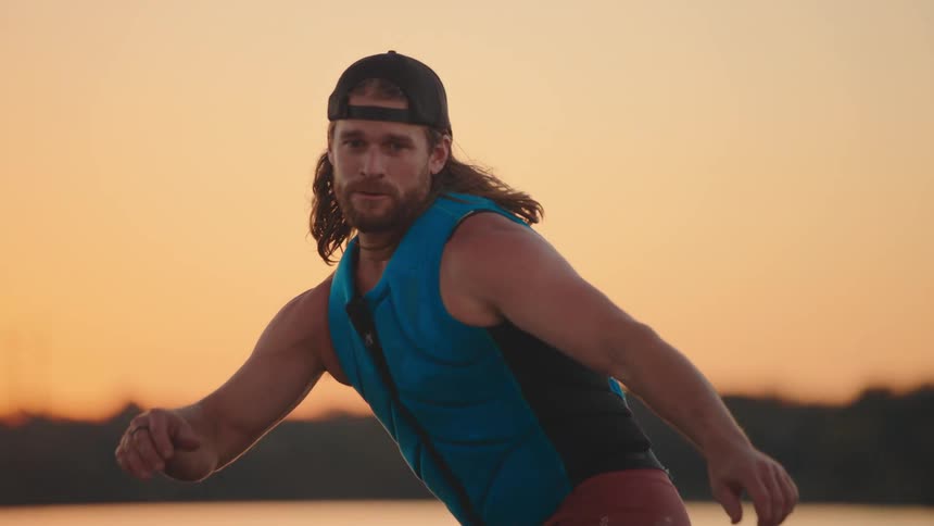 Man wearing backward cap and blue vest in motion outdoors against vibrant sunset backdrop